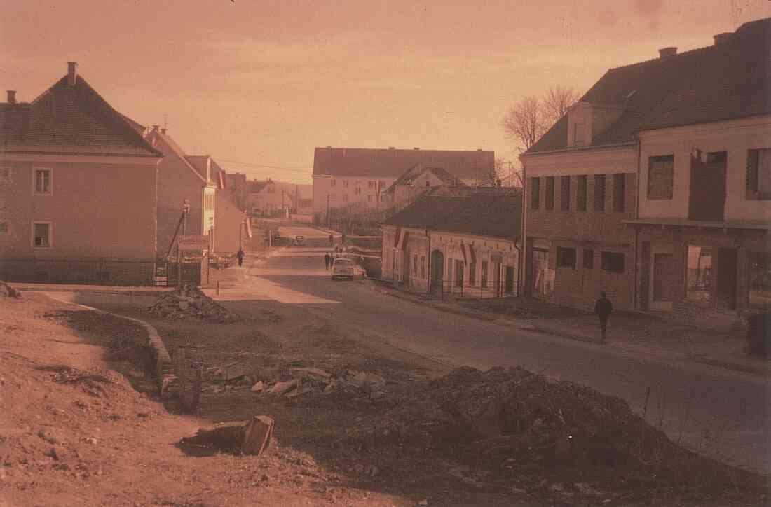 Platz vor dem Kastell und der Hauptschule mit den beflaggten Häusern der Familien Csar, Radanovits, Sabara, Konskr, Senninger, Bauer und Pieber